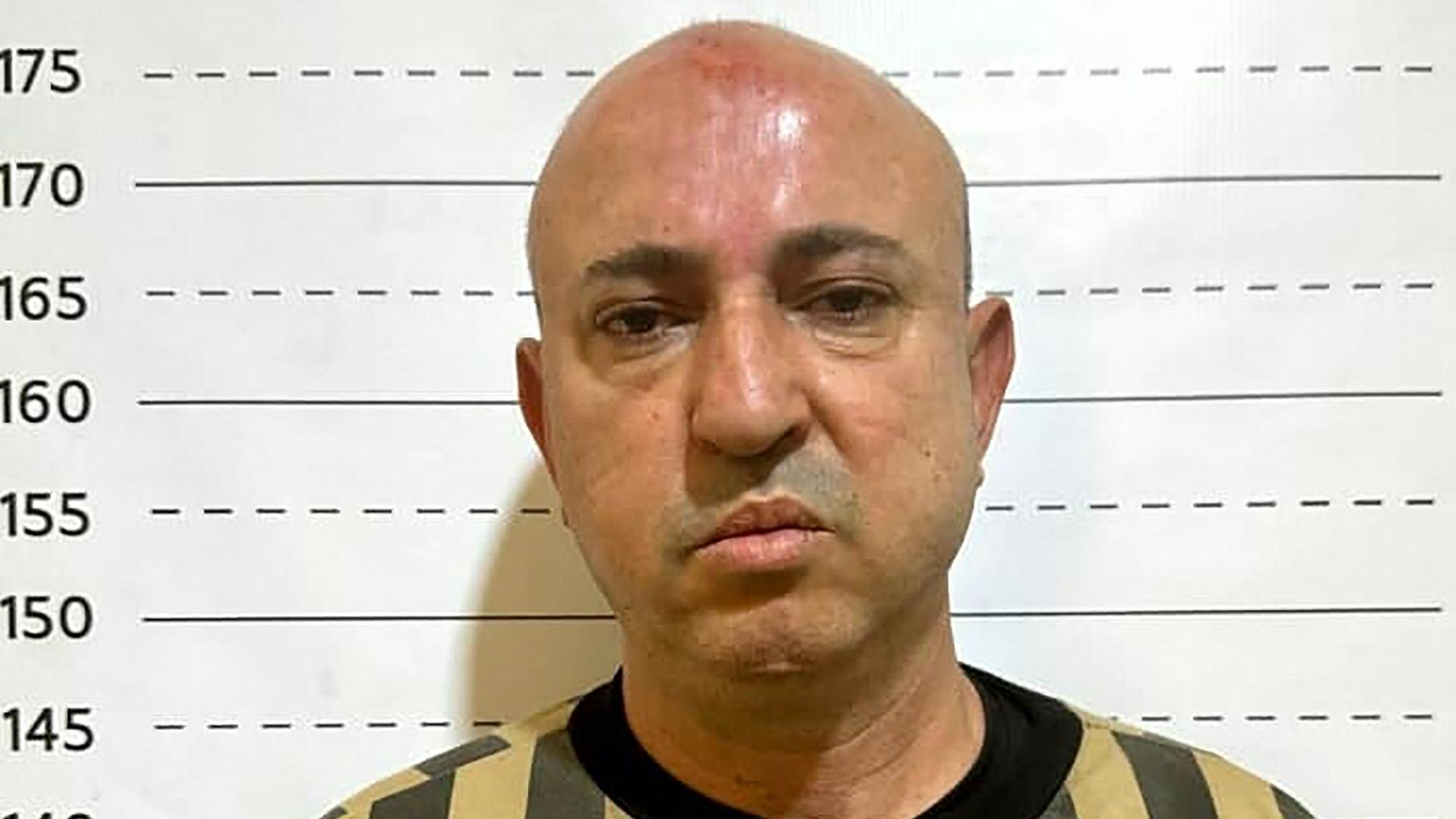 Wassim al-Assad steht in Gefängniskleidung vor einer Wand mit einem Größenmaß. Wassim al-Assad steht in Gefängniskleidung vor einer Wand mit einem Größenmaß.