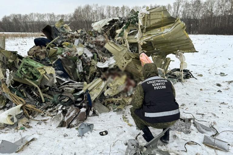 Ein Mann kniet vor Flugzeugtrümmern, die auf dem Boden liegen.