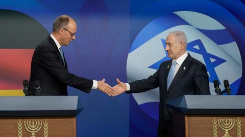 Bundeskanzler Friedrich Merz (l, CDU) schüttelt die Hand von Benjamin Netanjahu, Ministerpräsident von Israel. Im Hintergrund sieht man eine Flagge von Deutschland und eine von Israel.