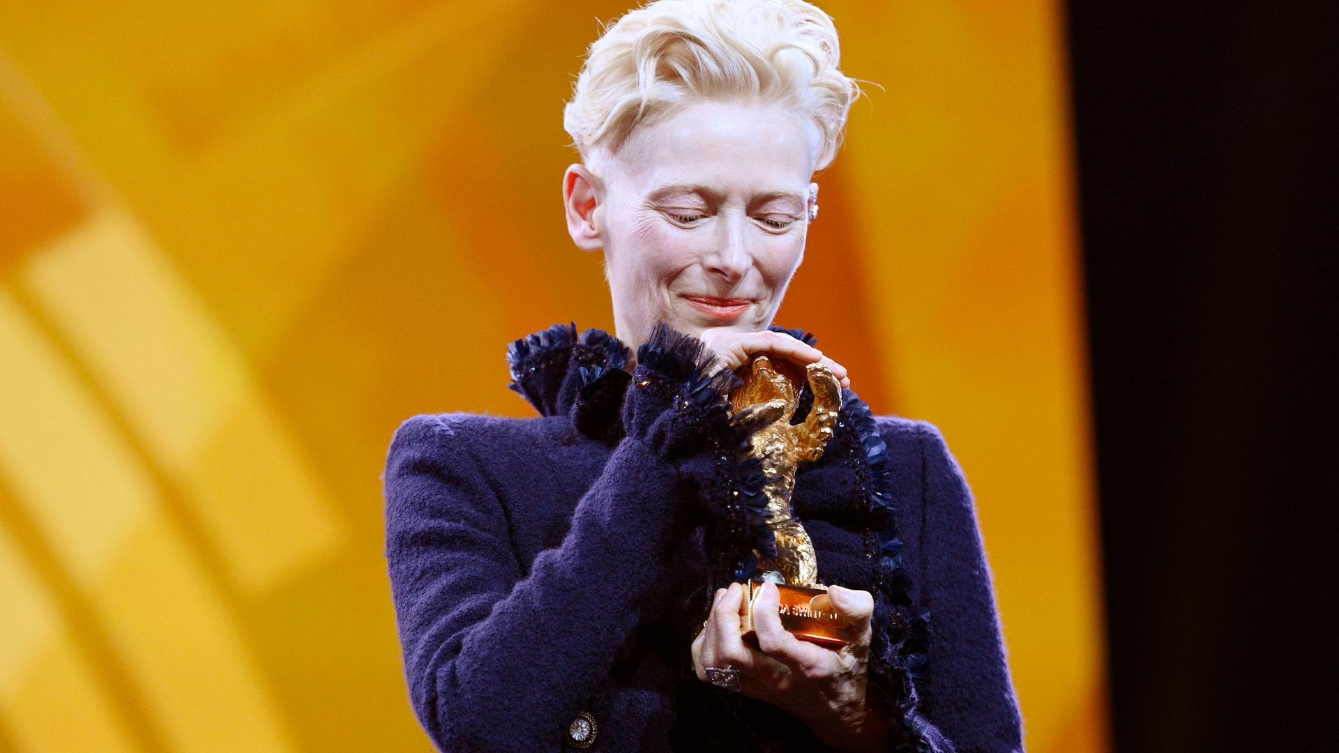 Tilda Swinton hält den Goldenen Ehrenbären für ihr Lebenswerk bei der Eröffnung der 75. Berlinale behutsam in den Händen und legt ihren Kopf darauf.