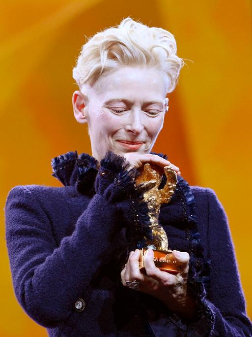 Tilda Swinton hält den Goldenen Ehrenbären für ihr Lebenswerk bei der Eröffnung der 75. Berlinale behutsam in den Händen und legt ihren Kopf darauf.