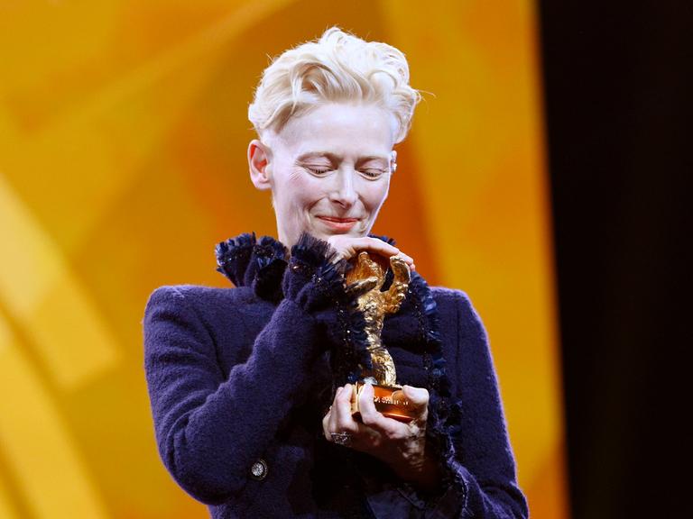 Tilda Swinton hält den Goldenen Ehrenbären für ihr Lebenswerk bei der Eröffnung der 75. Berlinale behutsam in den Händen und legt ihren Kopf darauf.