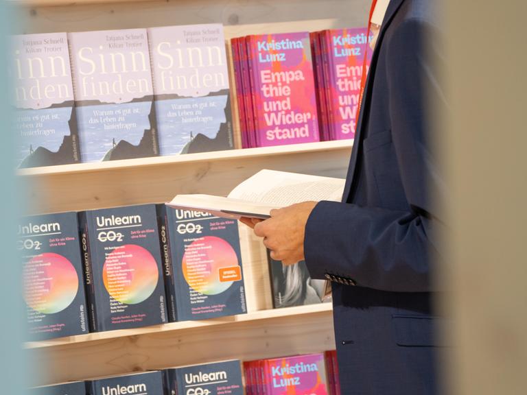 Eindrücke von der Frankfurter Buchmesse 2024. Im Anschnitt steht ein in einem Buch blätternder Mann vor einem Bücherregal mit Sachbüchern. 