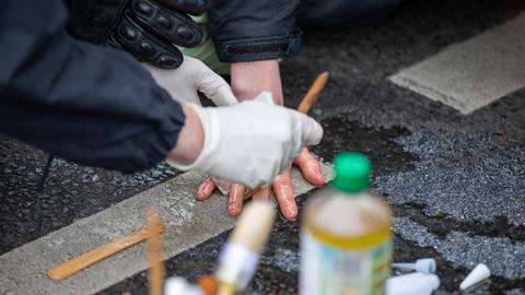 Klimaaktivisten blockieren eine Straße, indem sie sich mit Sekundenkleber an der Straße festkleben. Die Polizei löst sie mit Hilfe von Speiseöl.