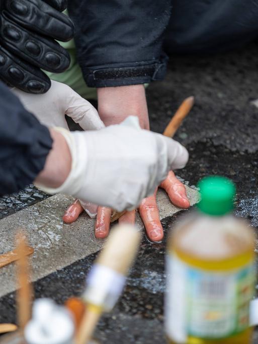 Klimaaktivisten blockieren eine Straße, indem sie sich mit Sekundenkleber an der Straße festkleben. Die Polizei löst sie mithilfe von Speiseöl.