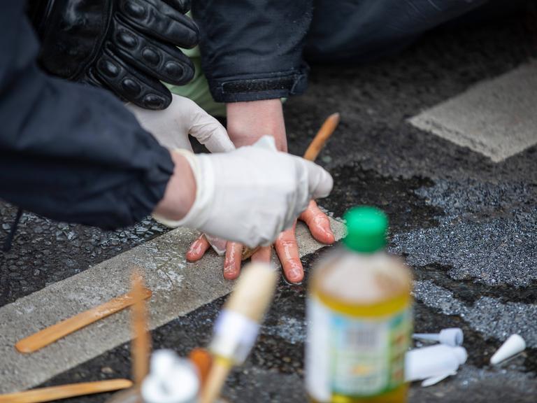 Klimaaktivisten blockieren eine Straße, indem sie sich mit Sekundenkleber an der Straße festkleben. Die Polizei löst sie mithilfe von Speiseöl.