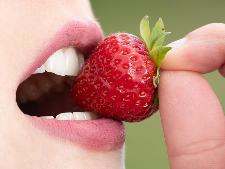 Zu sehen ist ein Mund, der genüsslich in eine große Erdbeere beißt. 