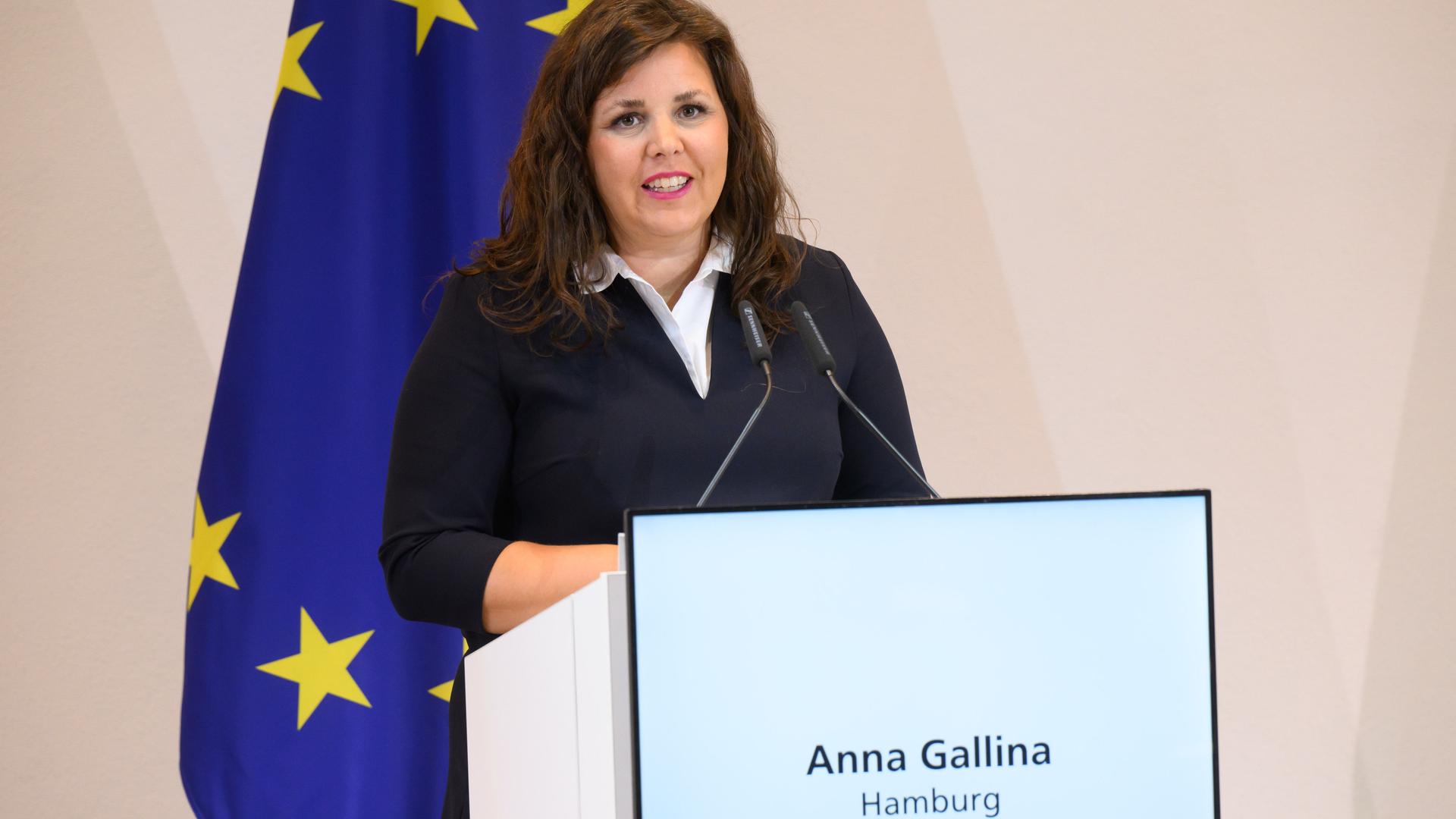 Anna Gallina (Grüne), Justizsenatorin Hamburg, steht an einem Rednerpult und spricht. Im Hintergrund ist eine Europa-Flagge zu sehen. 
