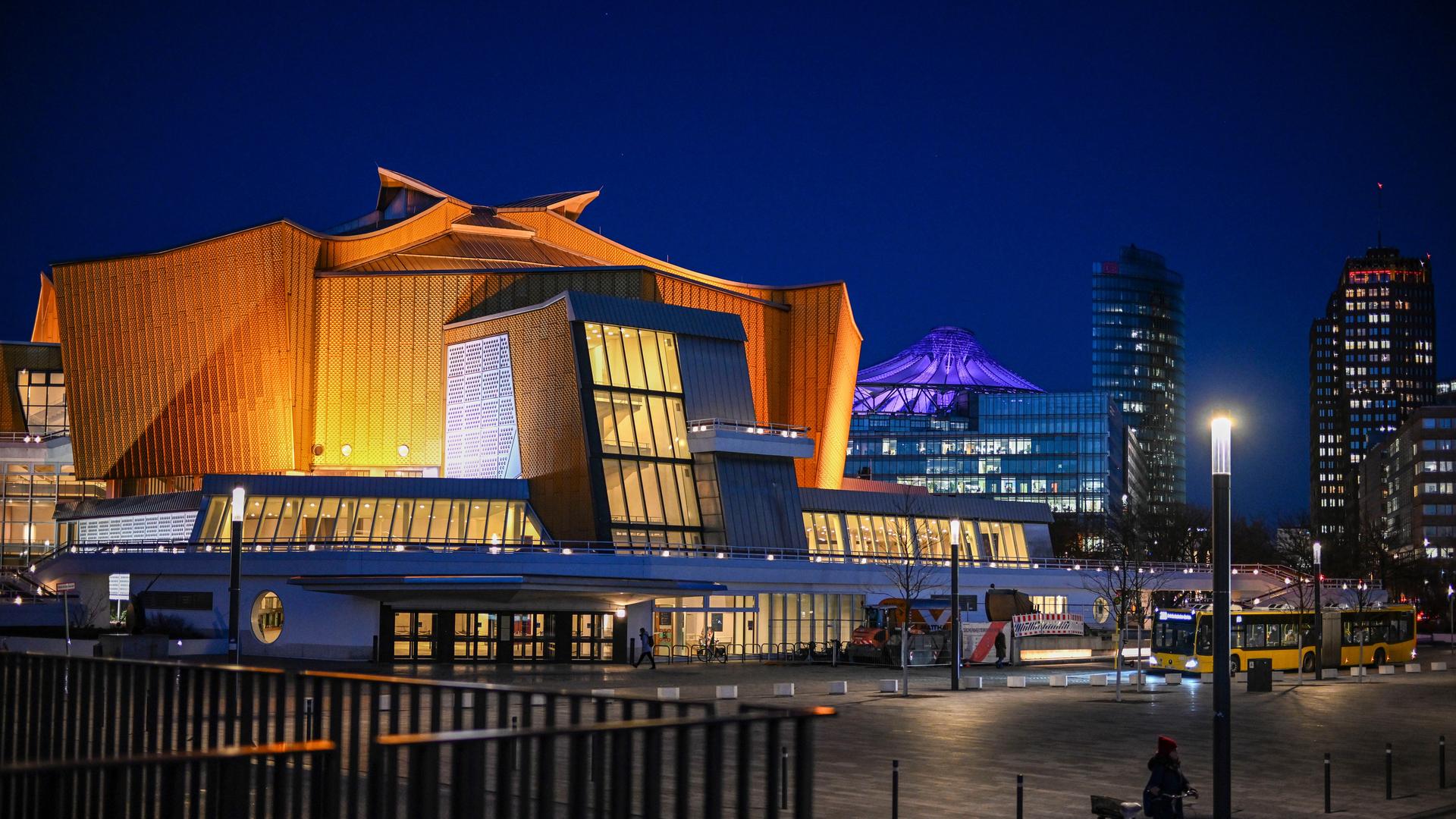 Blick auf die Berliner Philharmonie am Abend. Ein großes beleuchtetes Gebäude mit gold-gelbem geschwungenen Dach.