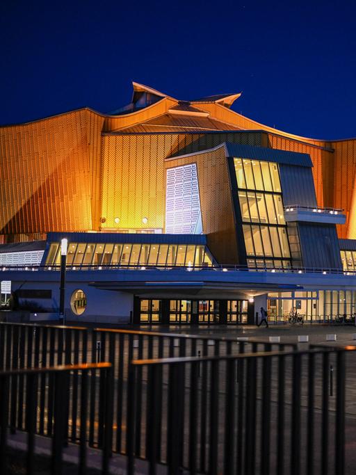 Blick auf die Berliner Philharmonie. Ein großes beleuchtetes Gebäude mit gelbem geschwungenen Dach.