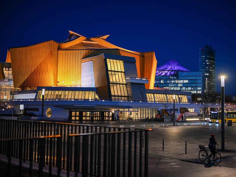 Blick auf die Berliner Philharmonie. Ein großes beleuchtetes Gebäude mit gelbem geschwungenen Dach.