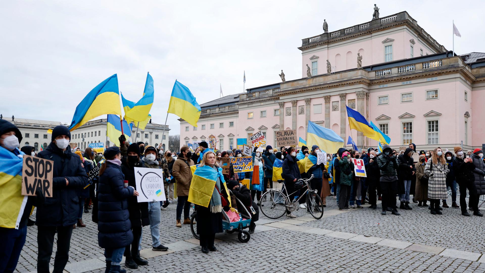 Demonstrierende auf dem Berliner Bebelplatz tragen blau-gelbe Fahnen der Ukraine und Plakate, auf denen sie ein Ende des russischen Krieges fordern.