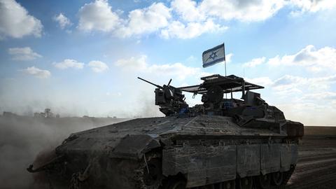 Ein israelisches Panzerfahrzeug mit Flagge wirbelt vor blauem Himmel Wüstensand auf.