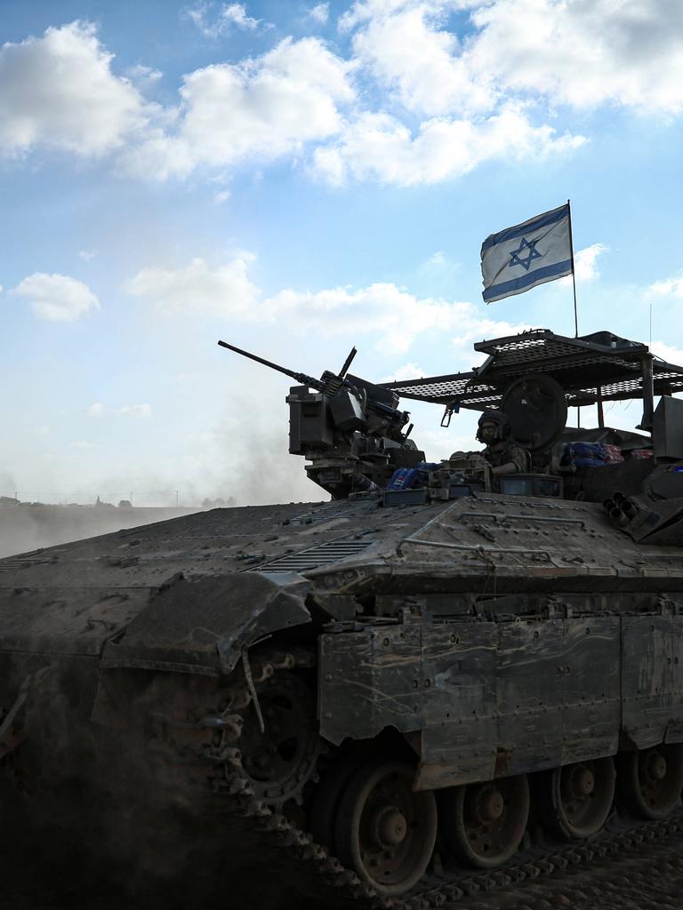 Ein israelisches Panzerfahrzeug mit Flagge wirbelt vor blauem Himmel Wüstensand auf.