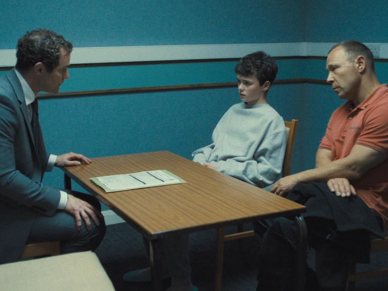 Filmszene aus "Adolescence": Ein Junge wird von der Polizei verhört. Neben ihm sitzt sein Vater.