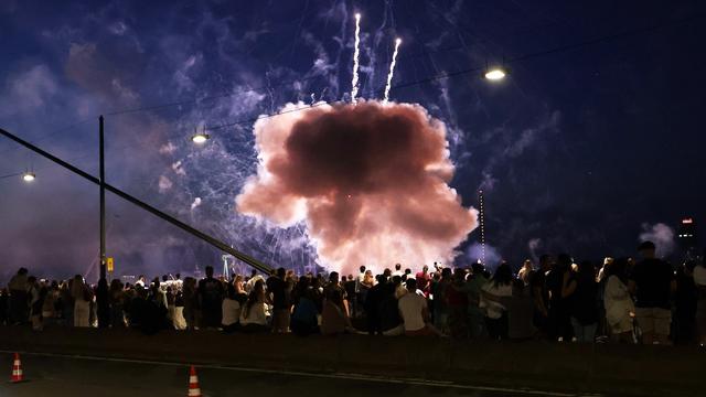 Blick auf eine Menschenmenge von hinten bei Nacht. Direkt vor ihnen ist eine hell erleuchtete Rauchwolke zu sehen.