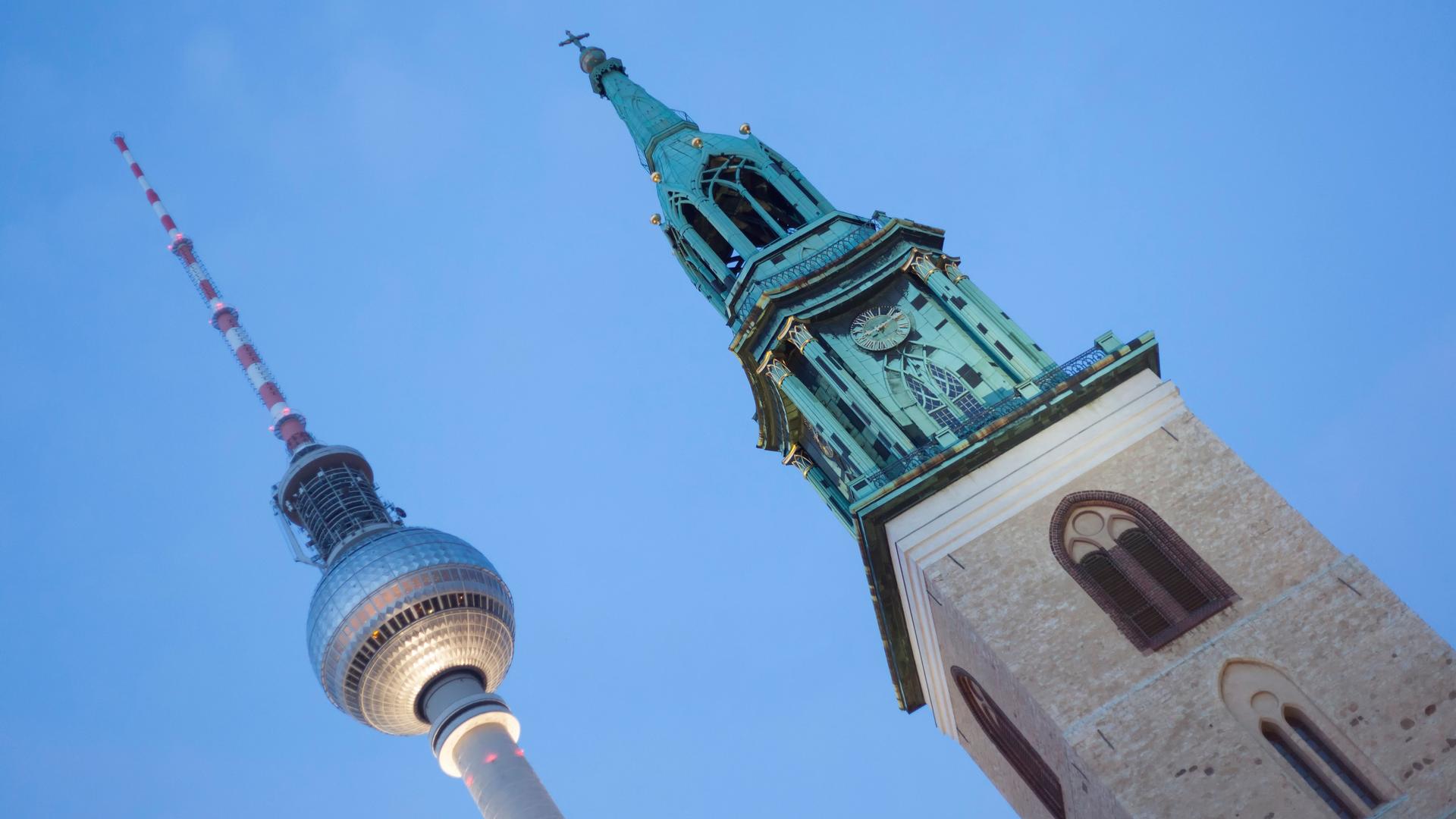 Das Bild zeigt den oberen Teil des Funkturms und den Kirchturm nebeneinander unter wolkenlosem blauem Himmel, fotografiert von unten. 