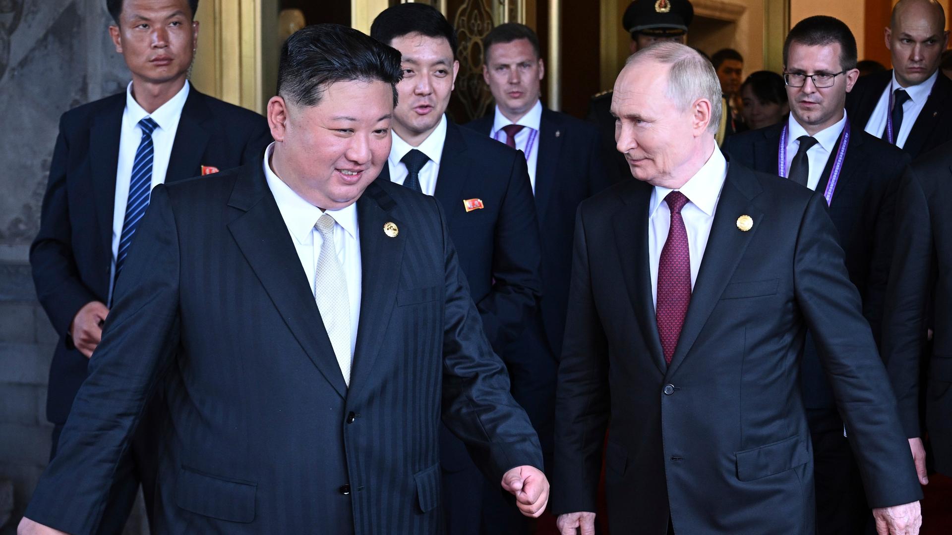 Der russische Staatschef Putin und Nordkoreas Machthaber Kim Jong Un gehen nebeneinander her, hinter ihnen noch mehrere Menschen. Der russische Staatschef Putin und Nordkoreas Machthaber Kim Jong Un gehen nebeneinander her, hinter ihnen noch mehrere Menschen.