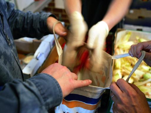 Zwei Hände füllen Lebensmittel in eine aufgehaltene Tasche. 