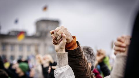 Menschen halten sich an den Händen auf der Großdemo gegen rechts in Berlin unter dem Motto "Wir sind die Brandmauer". Im Hintergrund ist der Reichstag zu sehen. 