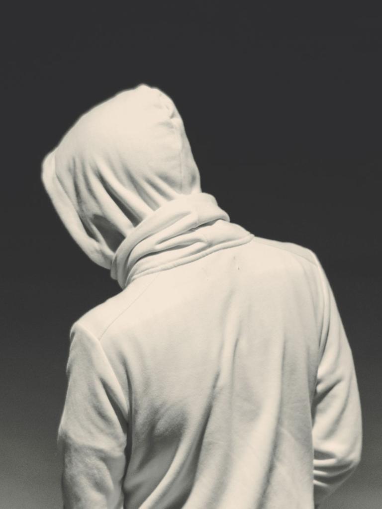 Ein junger Mann von hinten mit einem weißen Hoodie mit über den Kopf gezogener Kapuze