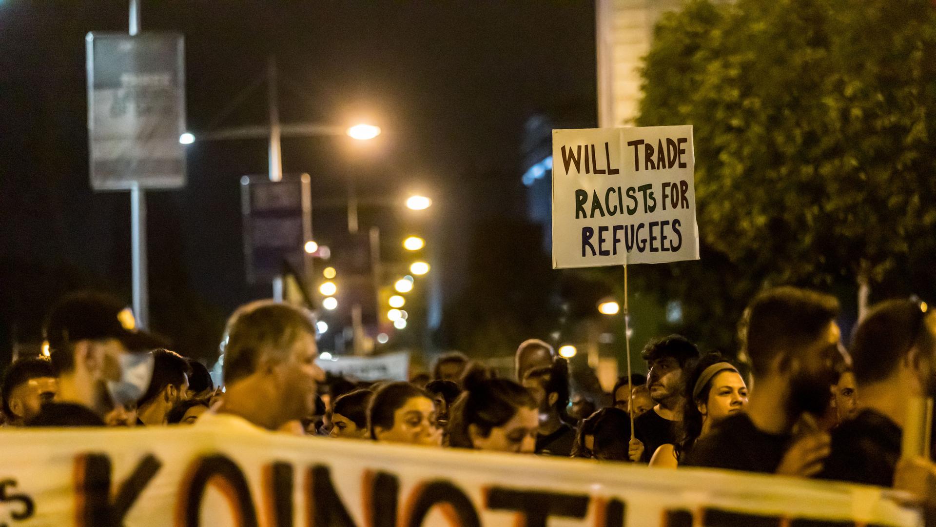 Es ist dunkel. Die Menschen tragen Schilder und Transparente. Auf einem Schild steht übersetzt: "Tausche Rassisten gegen Flüchtlinge".