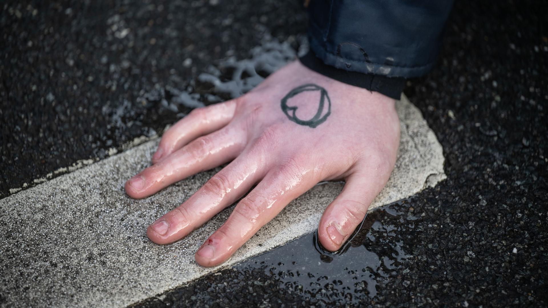 Ein Klimaaktivist der Gruppe "Letzte Generation" hat sich an einer Straße mit der Hand auf den Asphalt geklebt. Auf der Hand ist ein Herz.