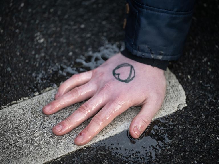 Ein Klimaaktivist der Gruppe "Letzte Generation" hat sich an einer Straße mit der Hand auf den Asphalt geklebt. Auf der Hand ist ein Herz.