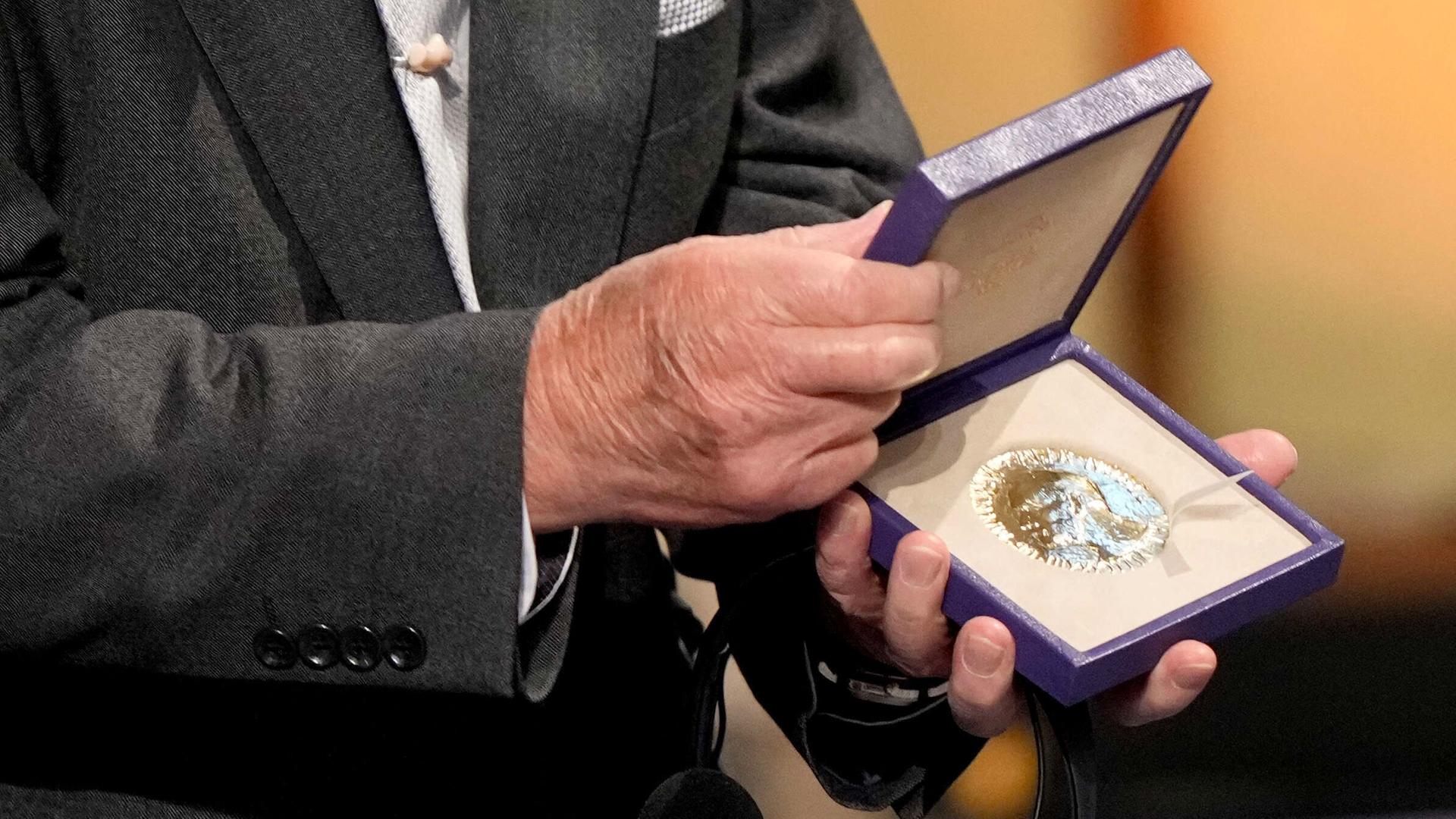 Die Hände eines Mannes halten die geöffnete Schatulle mit dem Preis. 