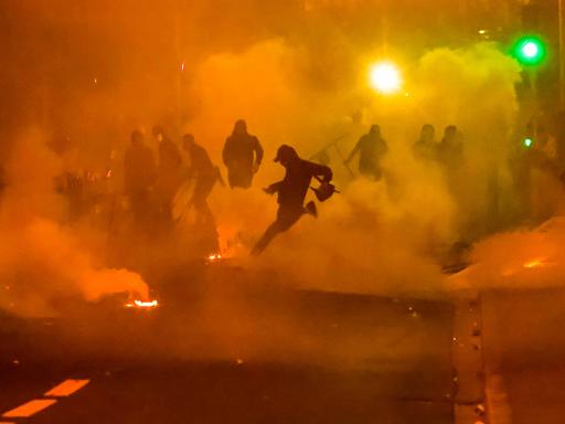 Im Gegenlicht einer rötlichen Tränengaswolke sind die Schatten von Demonstranten zu sehen. 