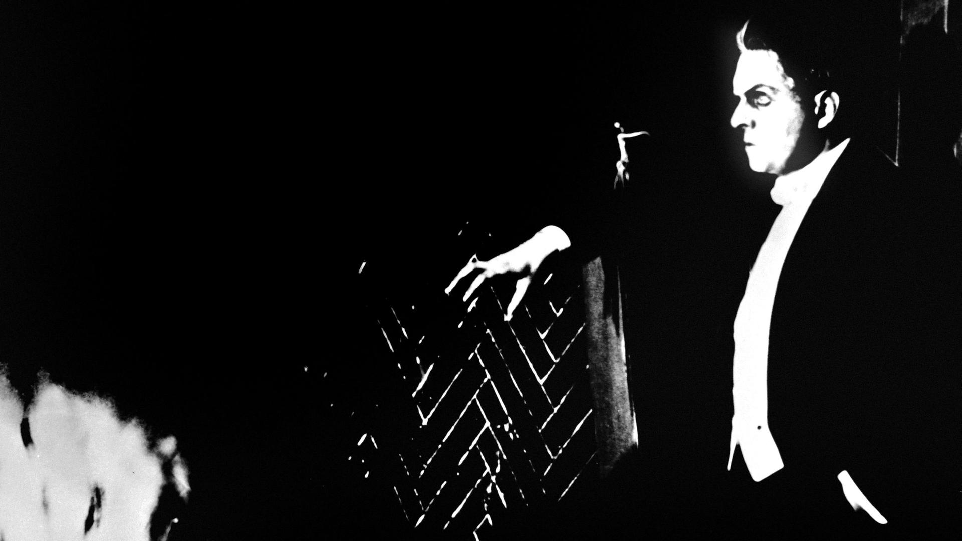 Der Schauspieler Rudolf Klein-Rogge ist in einer Szene aus Fritz Langs Stummfilm von 1922, "Dr. Mabuse, der Spieler" von der Seite zu sehen, um ihn herum ist es dunkel. Er macht einen düsteren Eindruck.

