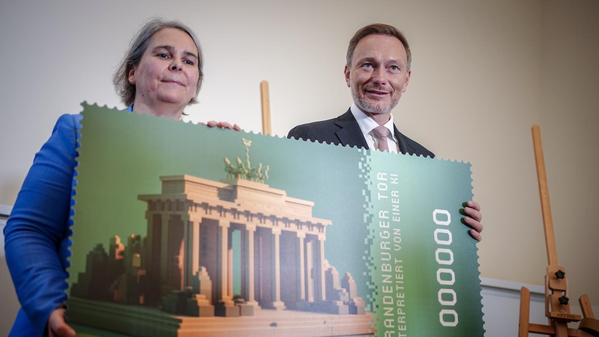 Christian Lindner (FDP), Bundesminister der Finanzen, und Nikola Hagleitner, Vorständin Post & Paket Deutschland, halten ein Plakat mit der ersten offiziellen Krypto-Briefmarke. Als Motiv zu sehen ist das Brandenburger Tor.