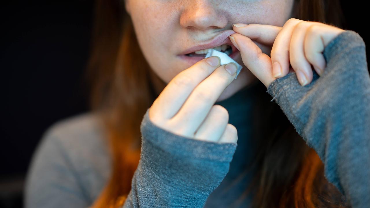 Eine junge Frau legt sich einen Nikotinbeutel an ihr Zahnfleisch. 
