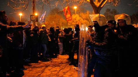 Demonstranten und Polizisten in robuster Montur stehen einander auf einem nächtlichen Platz gegenüber.