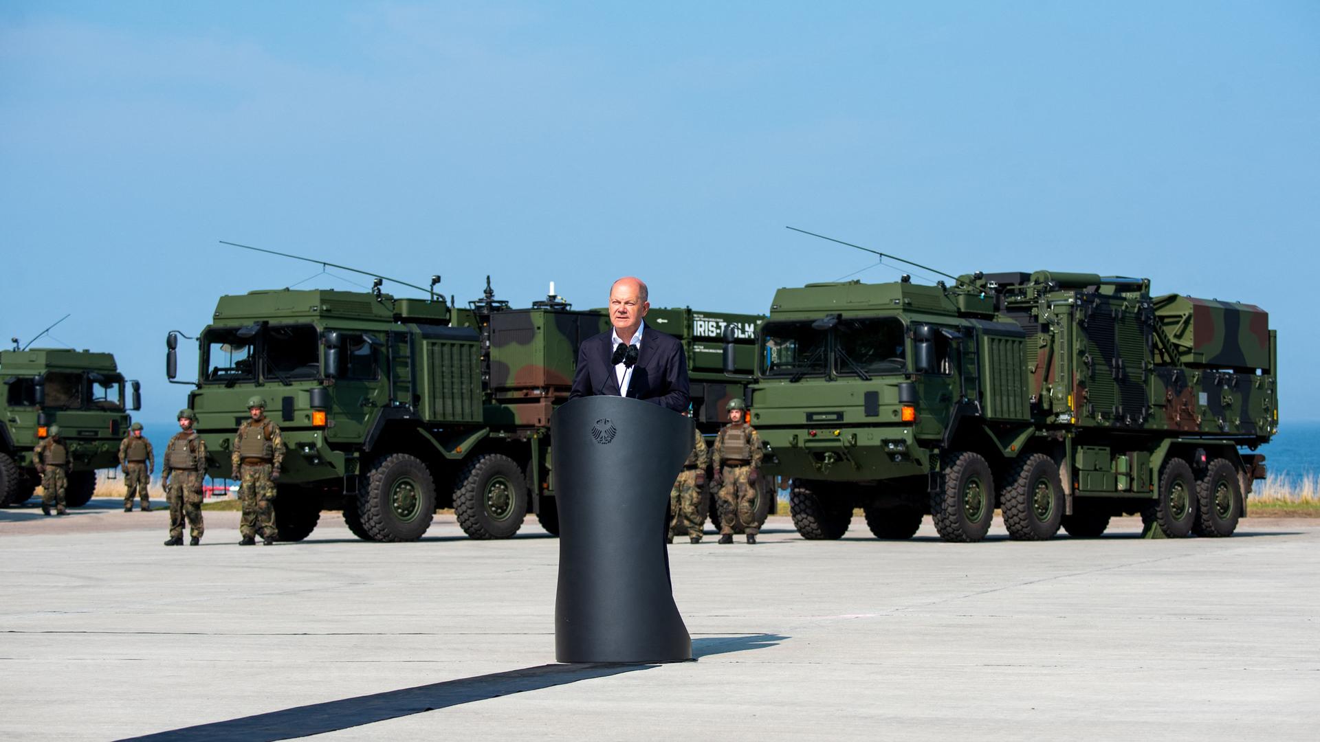 Bundeskanzler Scholz steht in Todendorf hinter einem Rednerpult. Hinter ihm stehen Soldaten und Militärfahrzeuge.