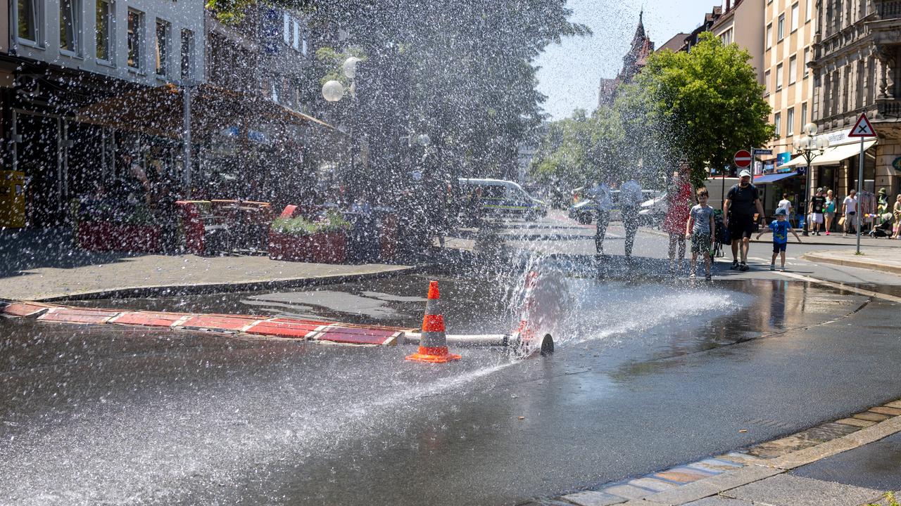 Über einen geöffneten Feuerwehrschlauch der Berufsfeuerwehr Nürnberg am Jakobsplatz wird Wasser zum Abkühlen versprüht bei sommerlicher Hitze. 