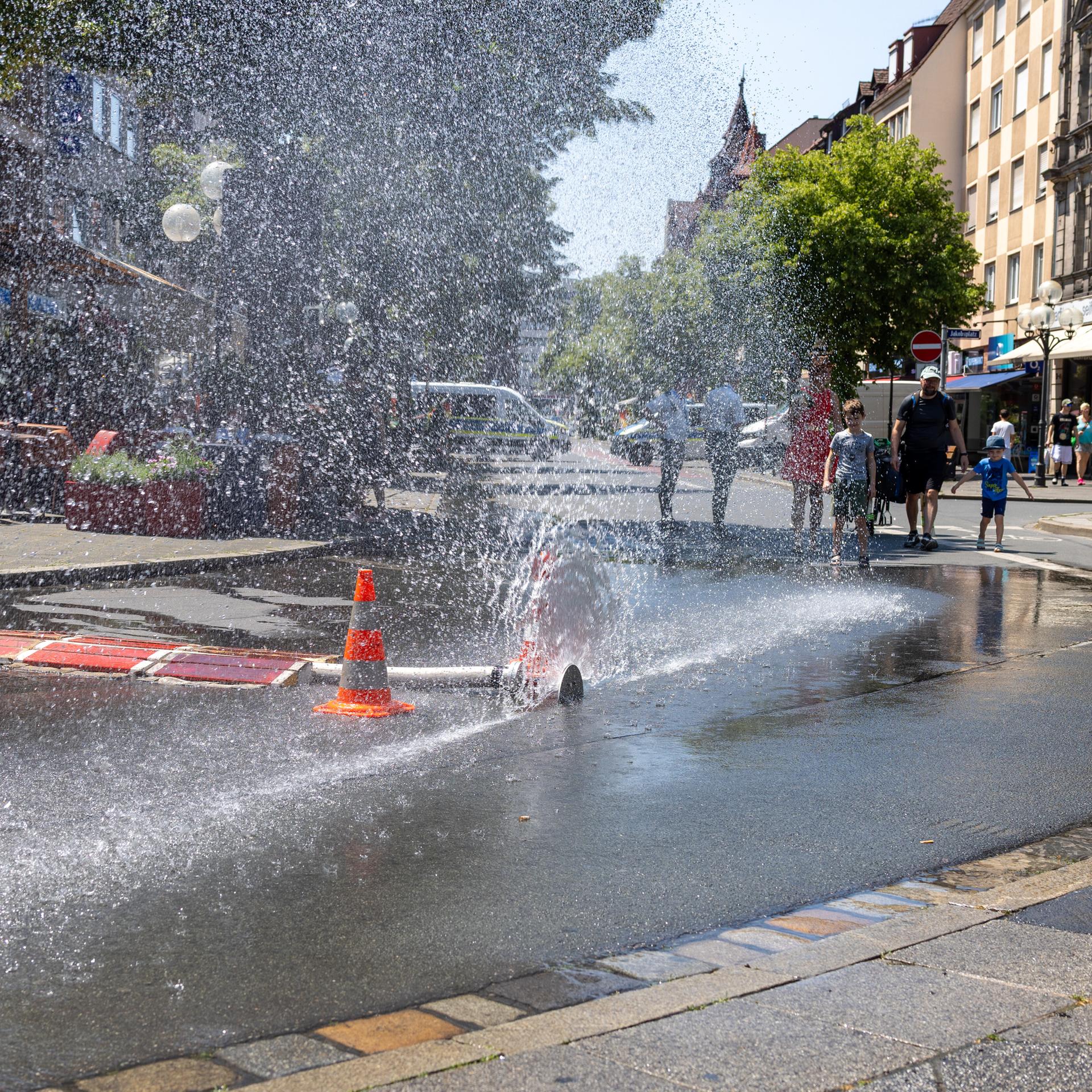 Über einen geöffneten Feuerwehrschlauch der Berufsfeuerwehr Nürnberg am Jakobsplatz wird Wasser zum Abkühlen versprüht bei sommerlicher Hitze. 