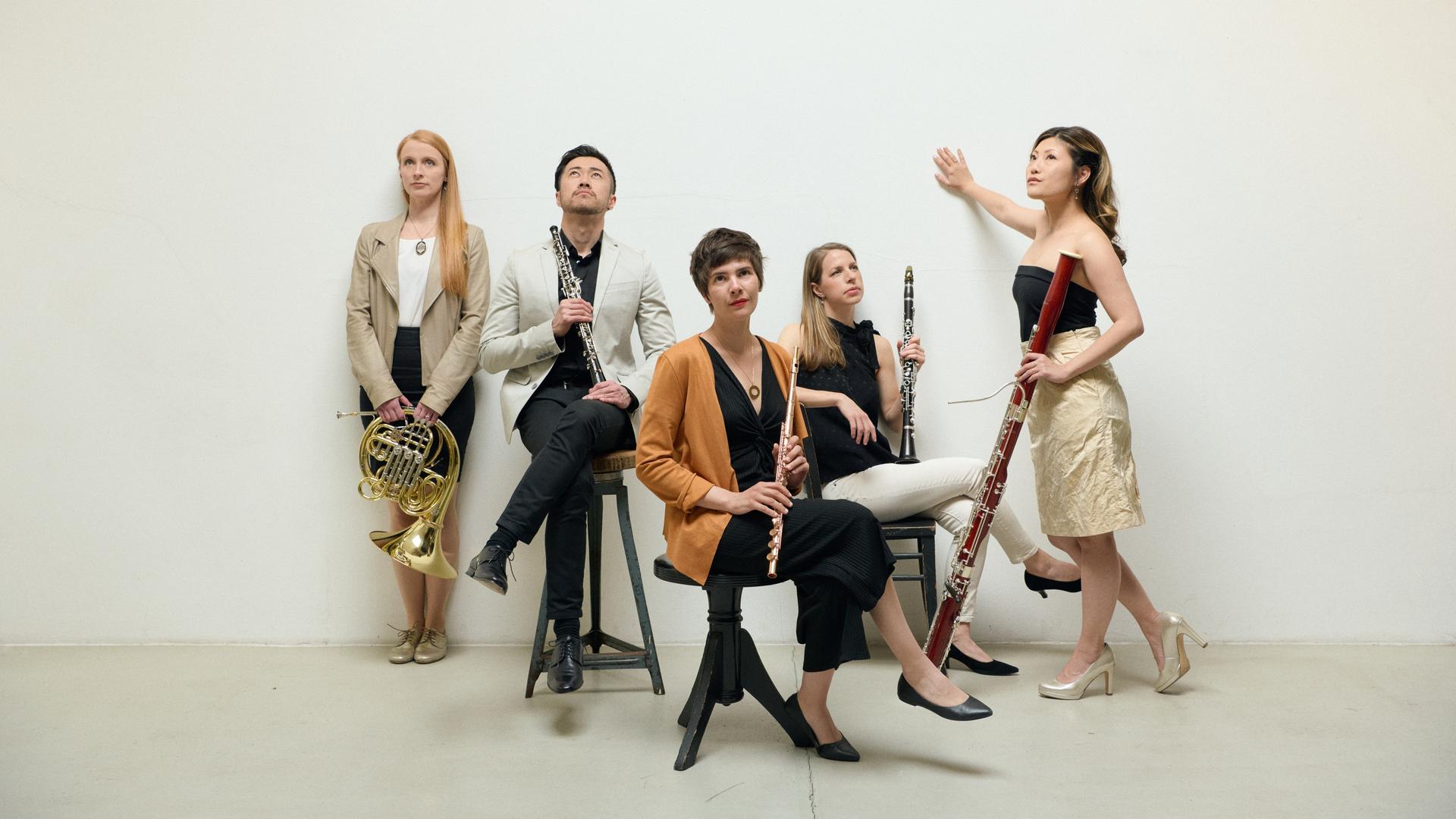 Vier Frauen und ein Mann sitzen oder stehen und alle halten ein Blasinstrument in der Hand.