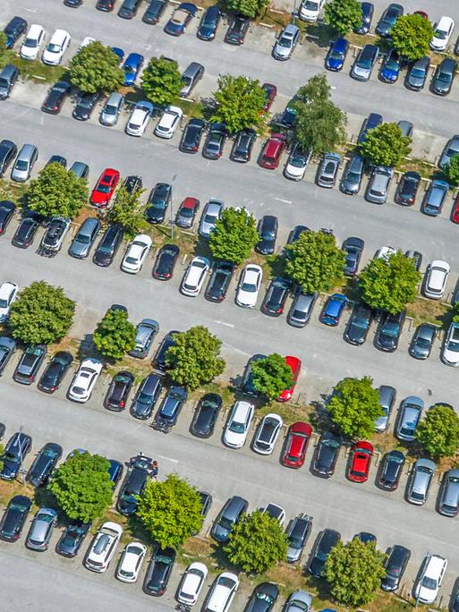  Blick von oben auf einen mit Autos komplett belegten Parkplatz.