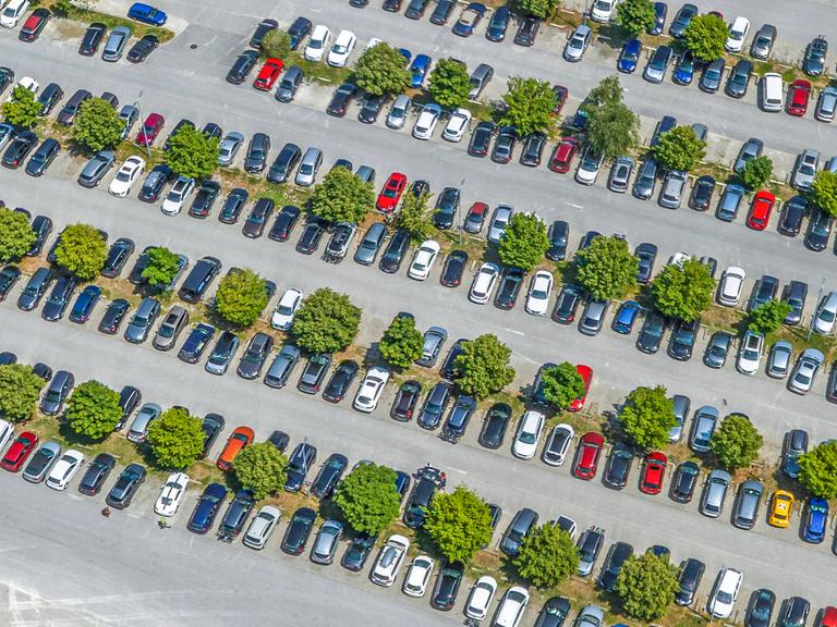  Blick von oben auf einen mit Autos komplett belegten Parkplatz.