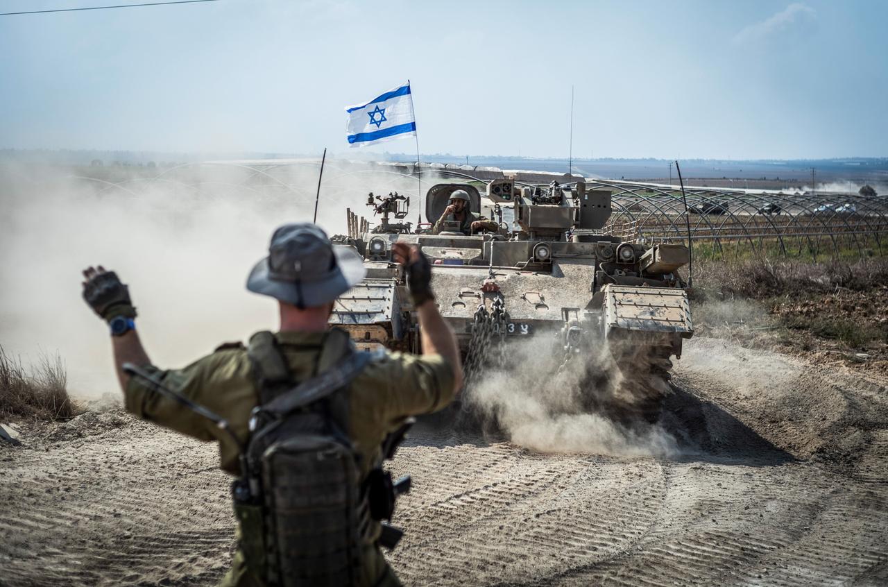 Zu sehen ist eine israelische Militärkolonne, die von einem Soldaten in eine Richtung gelotst wird.