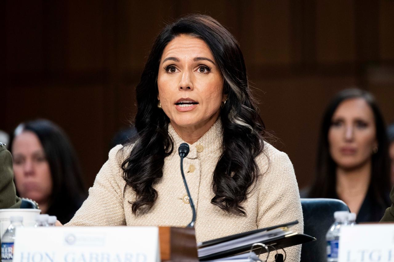 Gabbard sitzt an einem Tisch und spricht in ein Mikrofon. Sie trägt eine helle Jacke.