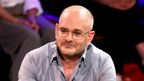 Das Foto zeigt Jonas Lüscher vom Oberkörper aufwärts. Er trägt ein graues Hemd, dessen oberster Knopf geöffnet ist. 