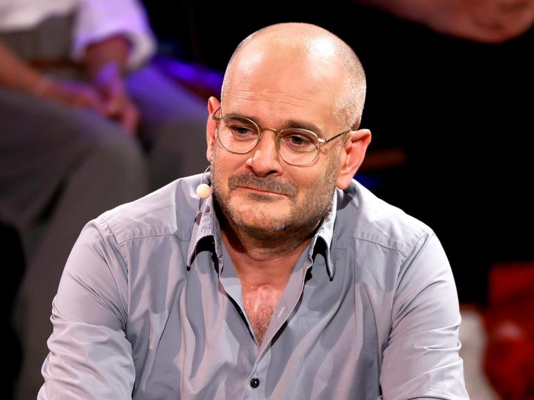 Das Foto zeigt Jonas Lüscher vom Oberkörper aufwärts. Er trägt ein graues Hemd, dessen oberster Knopf geöffnet ist. 