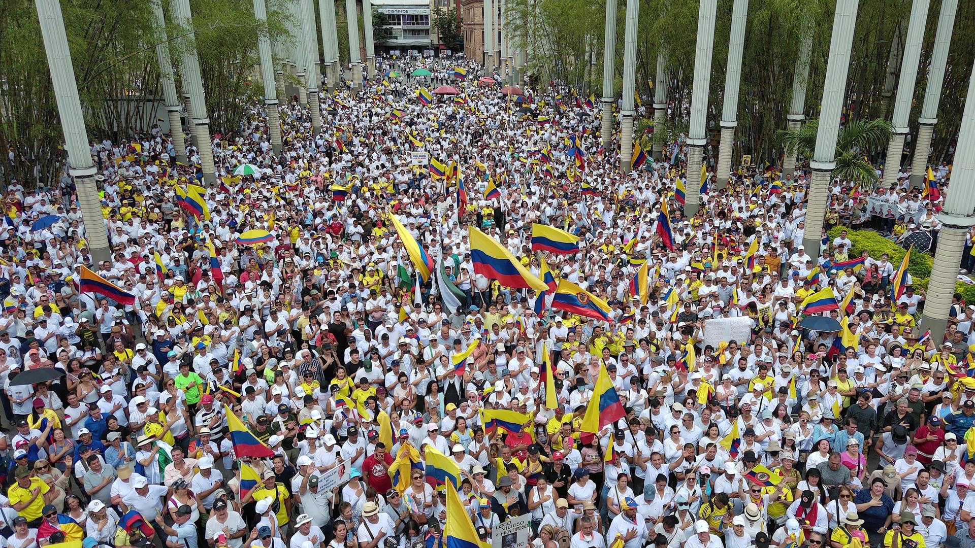 Eine riesige Menschenmenge füllt eine Straße bei einer Demonstration in Medellin in Kolumbien. Sie schwenken viele Fahnen.