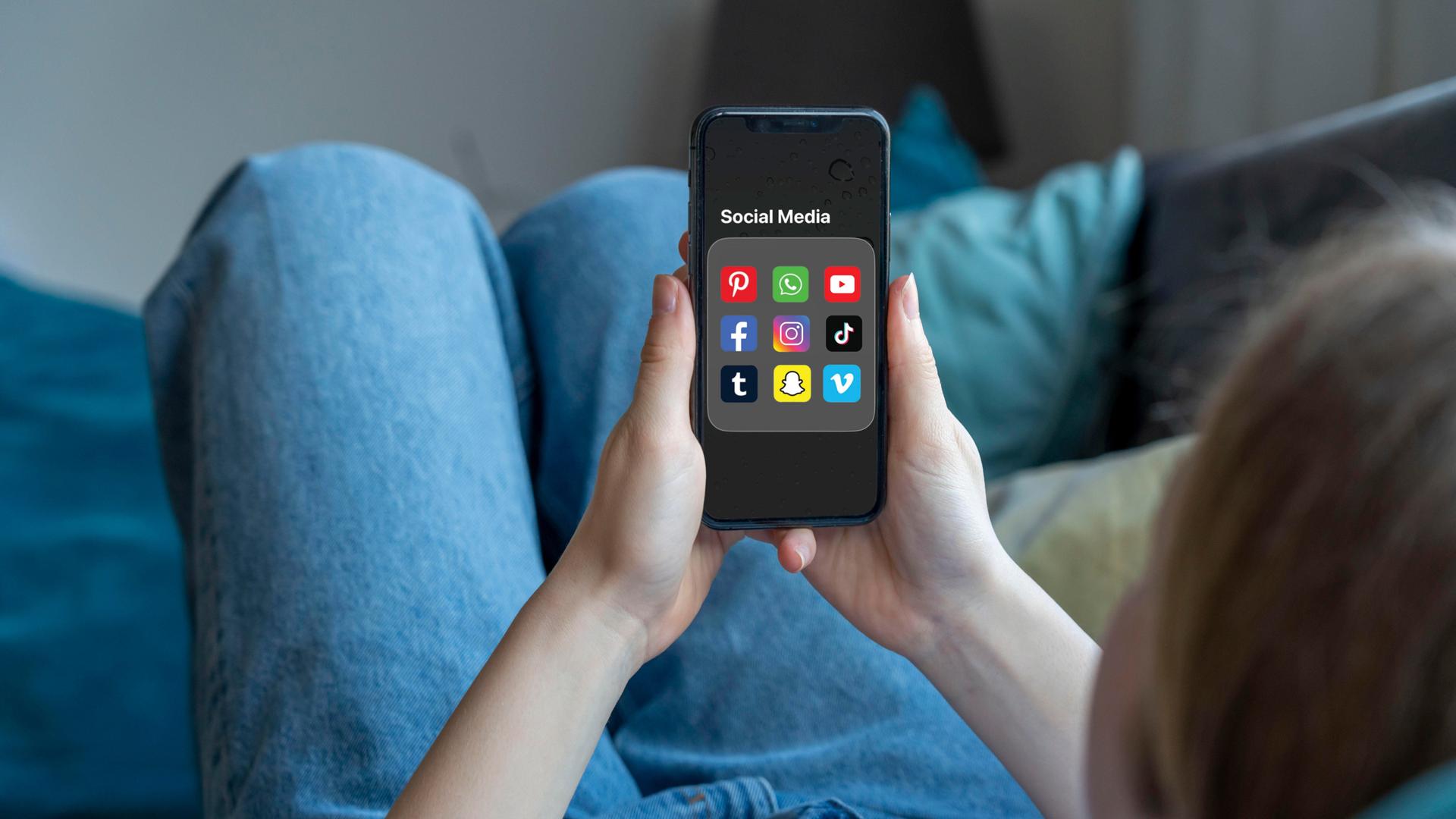Eine Person hält ein Handy in der Hand. Auf dem Handy-Bildschirm sind mehrere Apps für Soziale Medien zu sehen.