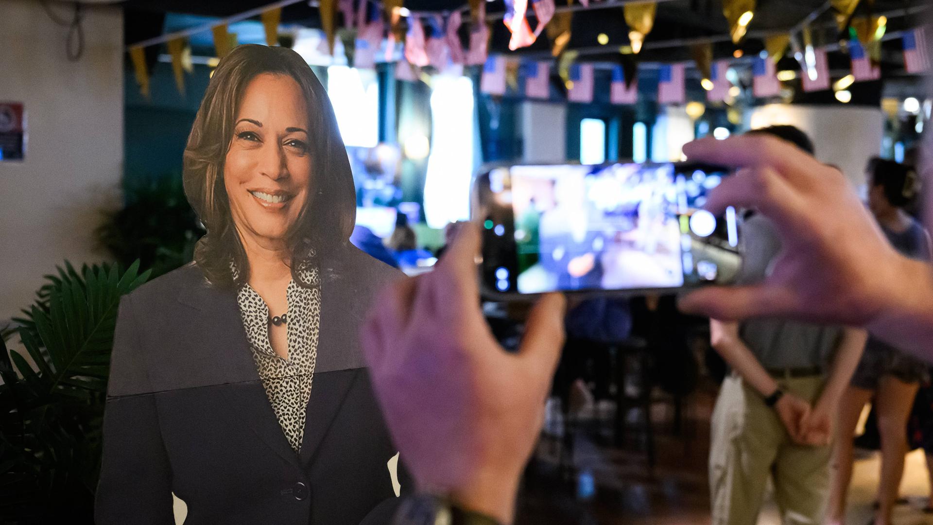 Auf einer Wahlparty steht ein Pappaufsteller von Kamala Harris. 