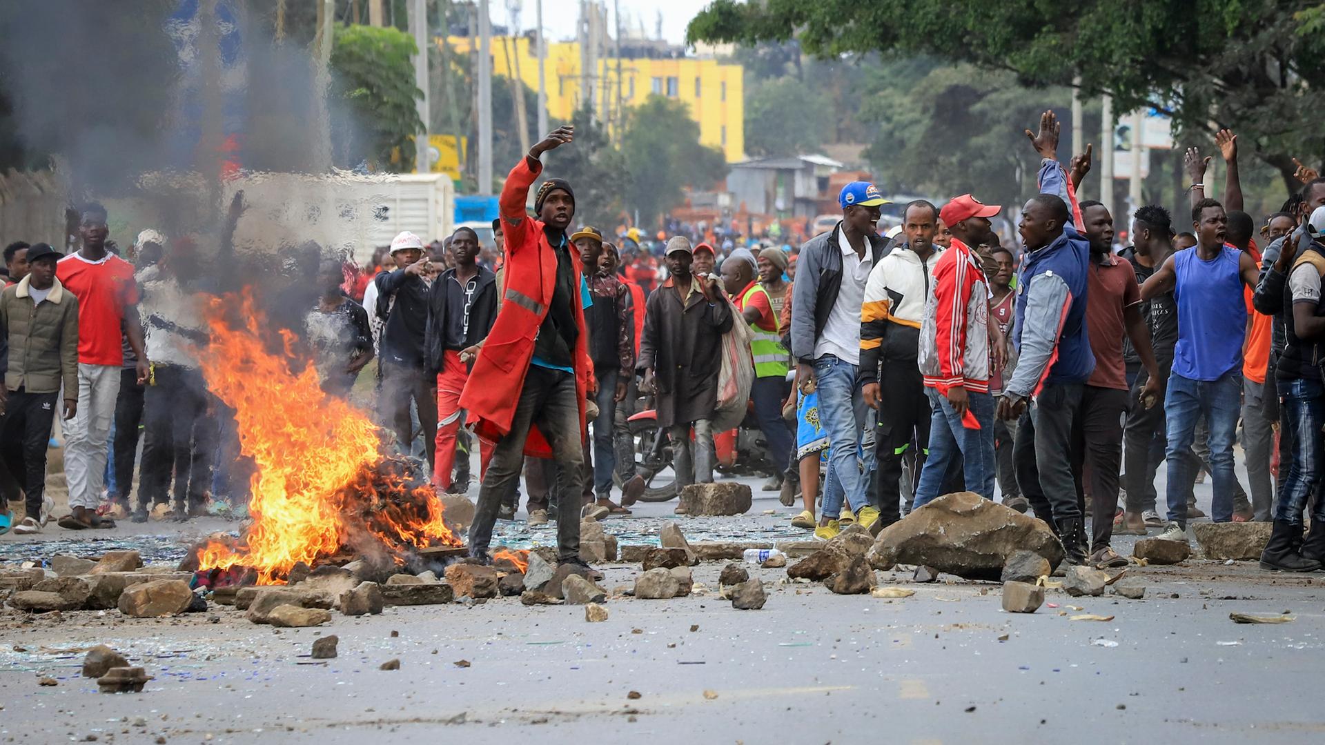 Menschen stehen hinter einer Reihe von Steinbrocken auf einer Straße und brennenden Autoreifen. Einige strecken die Arme in die Höhe.