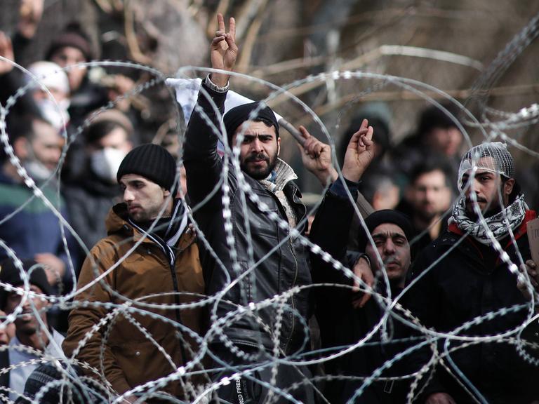 Migranten stehen hinter einem Maschendrahtzaun an der griechischen Grenze.