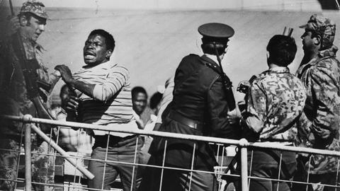 Während eines Anti-Apartheid Protests im Soweto Township in Südafrika rennt einer der Protestierenden in Richtung einer Absperrung während Polizisten und Soldaten versuchen, ihn aufzuhalten.